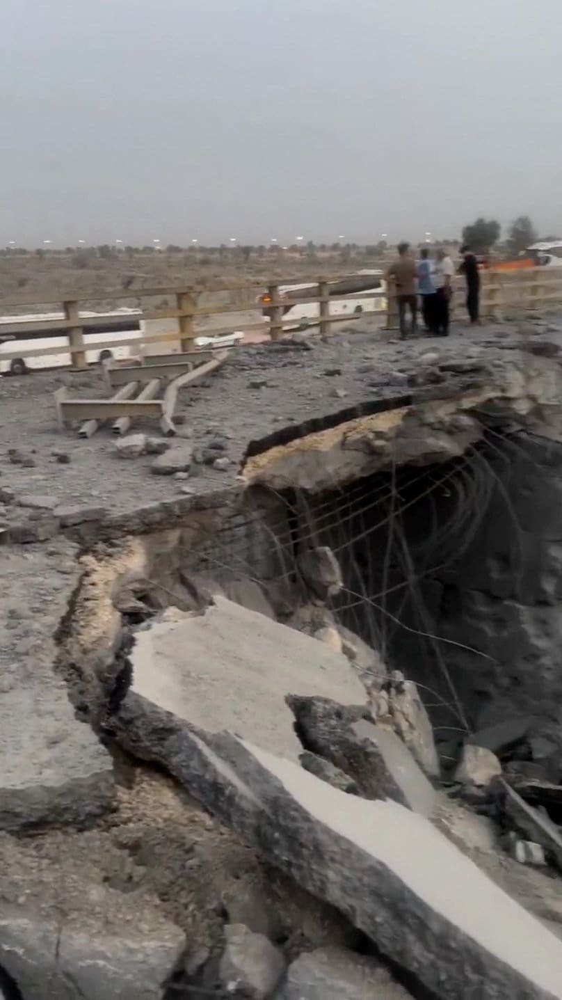 People stand near a damaged portion of a bridge in the aftermath of a strike, in Bandar Khamir